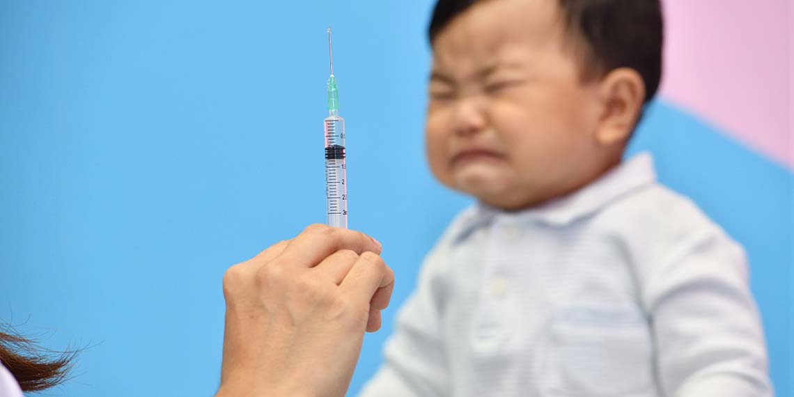 Ein kleiner Junge schließt die Augen vor der Spritze und verzerrt sein Gesicht weil er Angst vorm Impfen hat